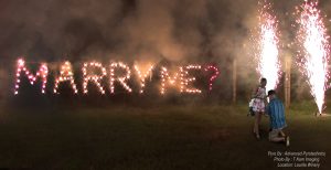 A wedding proposal featuring the couple and a fire writing set piece that says Marry Me? that was designed by Advanced Pyrotechnics, a fireworks company.
